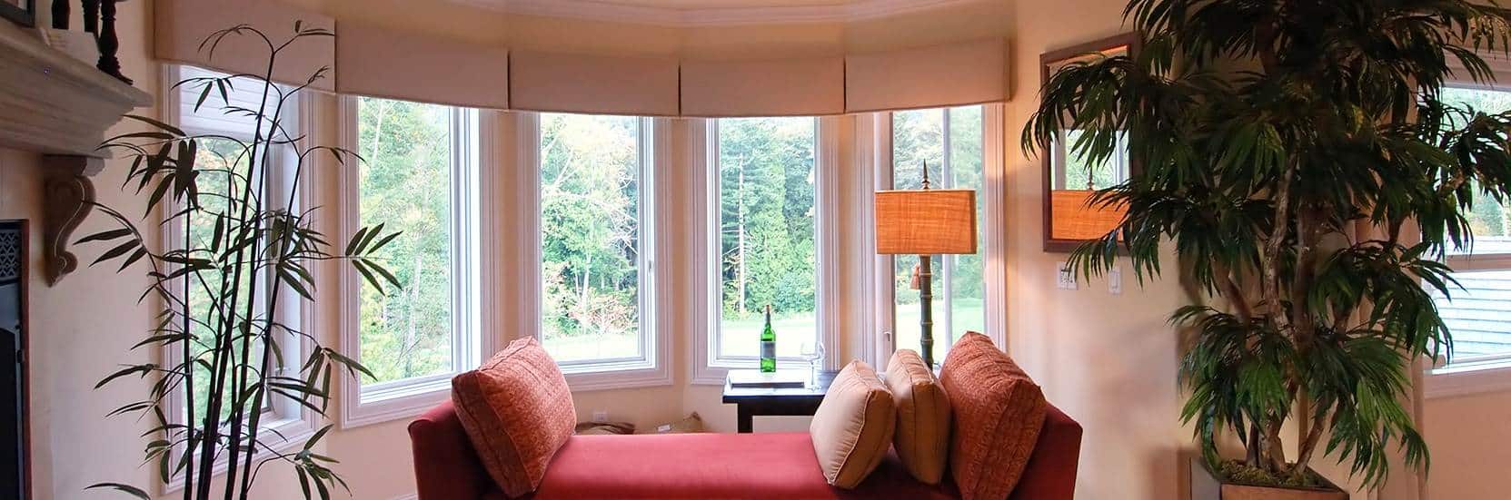 A living room with a couch and a plant near the bow window.