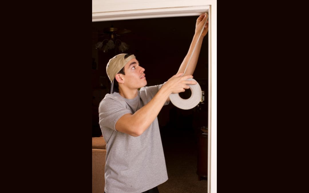 weatherstripping-and-door-sweeps-improve-energy-efficiency - A man applying weather stripping to a door frame.