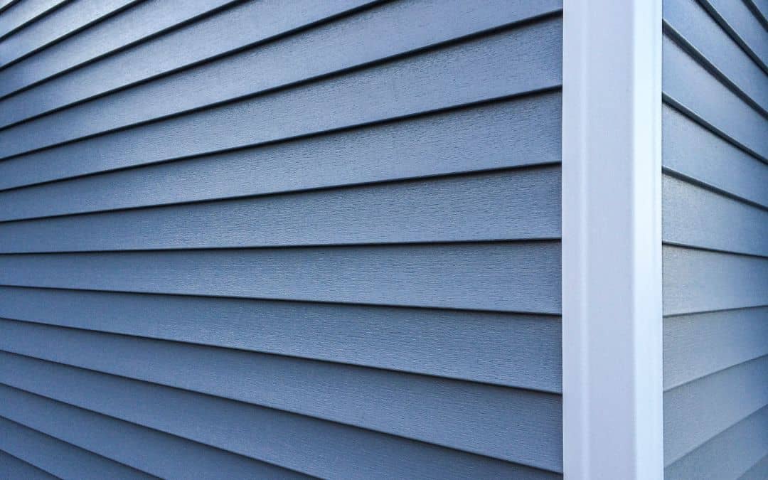 Close-up of a house corner featuring blue horizontal vinyl siding on both walls, with a white trim at the corner intersection.