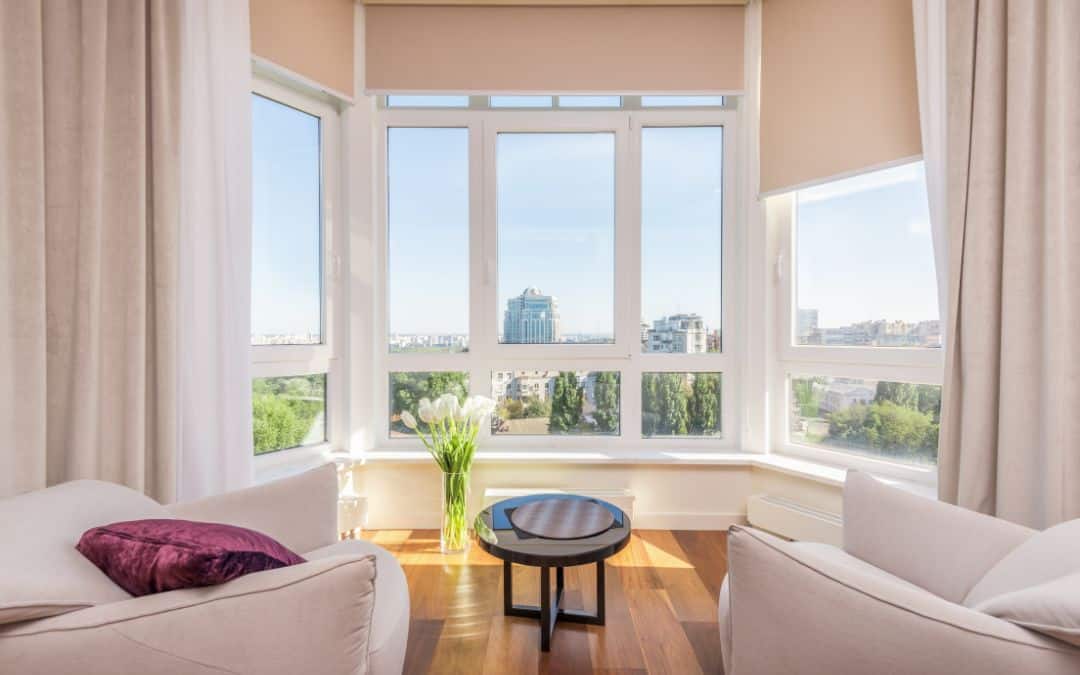 bay windows A bright living room with large bay windows offers a city view. Two chairs with cushions flank a small round table. A vase of flowers sits by the window.